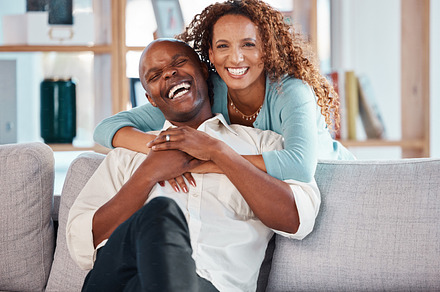 Couple, hug and laughing on sofa portrait in home living room, bonding and having fun. Interracial, love and funny black man and woman on couch embrace, happiness and enjoying quality time together., a Photo by Peopleimages.com