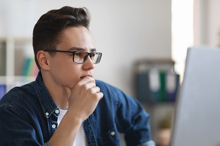 Portrait Of Pensive Young Male Entrepreneur In Eyeglasses Sitting At Workplace, a Photo by Prostock-Studio