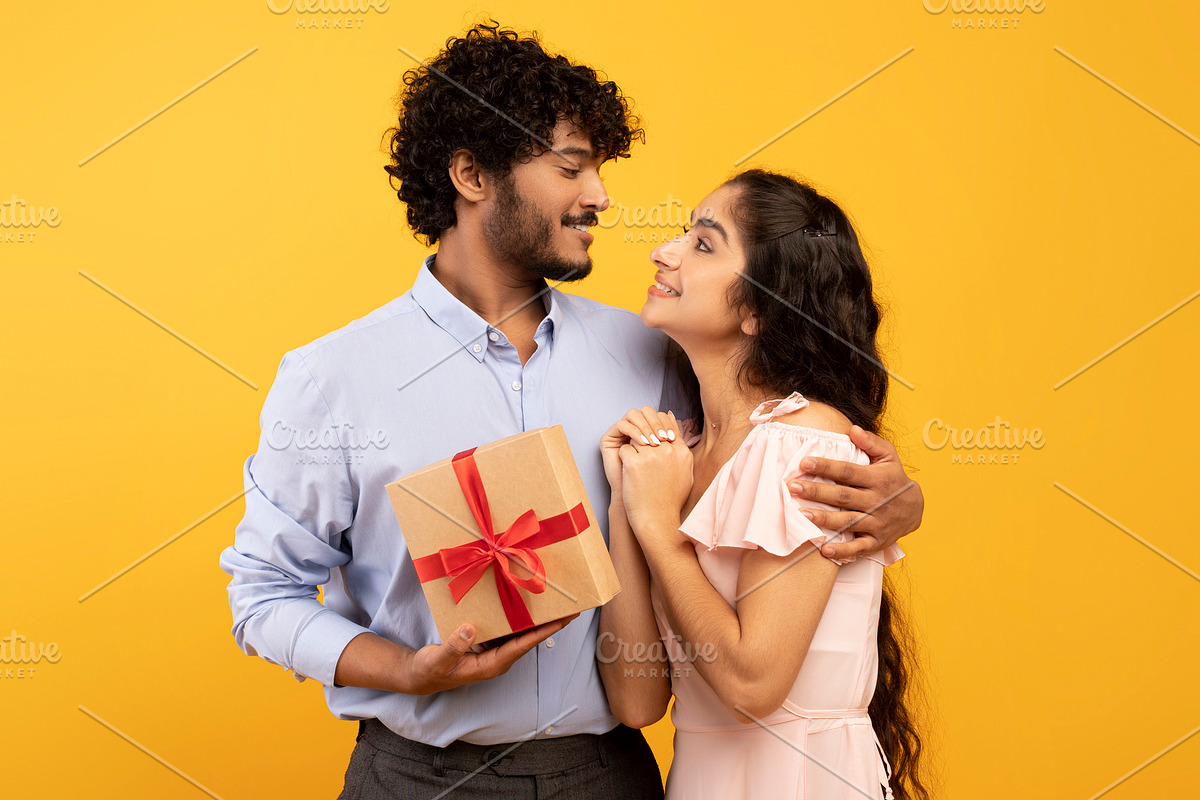 Celebration concept. Loving indian couple embracing and man holding wrapped gif, a Photo by Prostock-Studio (Photo 2 of 3)
