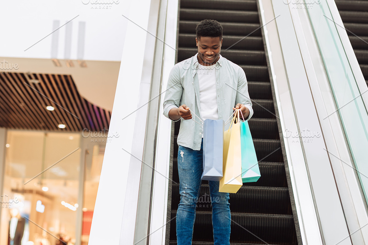 Happy black man holding shopping bags looking inside, a Photo by Prostock-Studio (Photo 1 of 3)