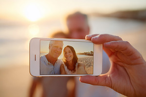 Couple enjoying a sunset selfie with AR filter effects on the beach in warm lig, a Photo by AlyaAnd