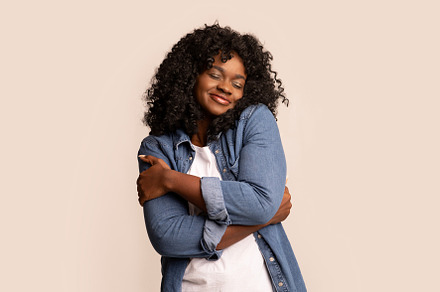 Joyful black lady in love hugging herself, a Background Photo by Prostock-Studio