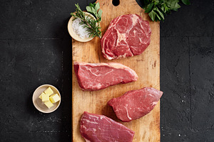 Raw rib-eye, roast beef, flank and rump steak on a wooden cutting board with he, a Food & Drink Photo by Asya Nurullina