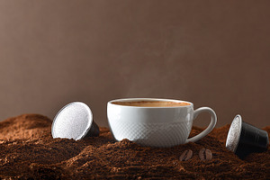 Espresso cup on ground coffee with capsules around front view, a Food & Drink Photo by Davizro's Market