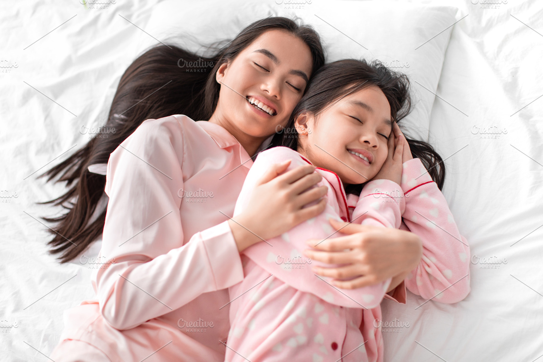 Satisfied japanese millennial woman hugging teen girl in pajama lie on bed and, a Photo by Prostock-Studio