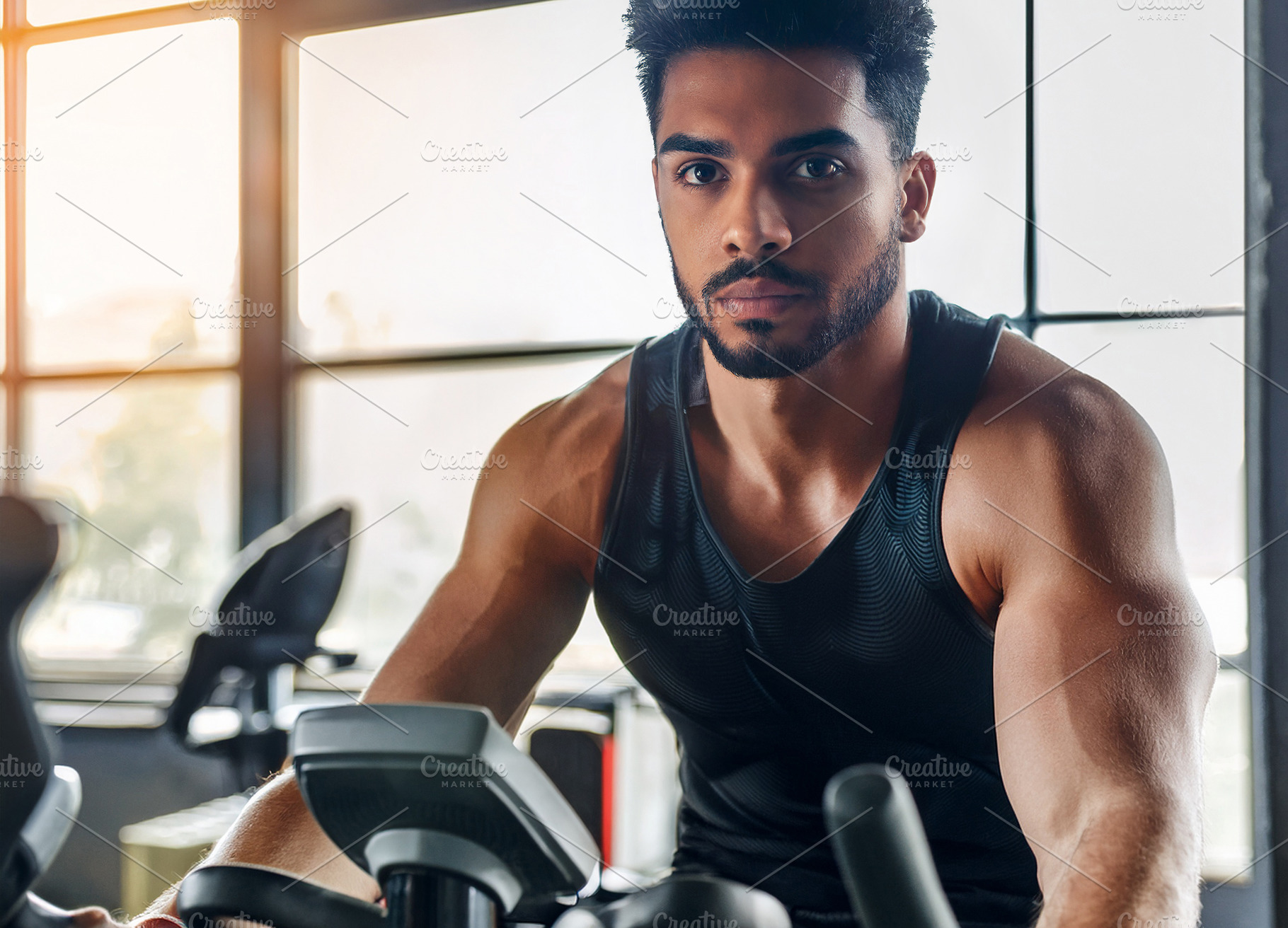 Muscular young man using a stationary bike in a gym, a Sports & Recreation Photo by Davizro's Market