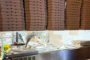 Stacked pizza boxes in a pizzeria kitchen showcasing preparation and storage, a Photo by AS photostudio