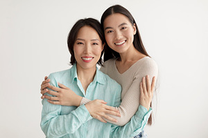 Joyful young Asian woman and her senior mother hugging and smiling at camera on, a Photo by Prostock-Studio