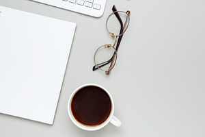 Comfortable workspace setup with coffee cup, keyboard, glasses and notebook sha