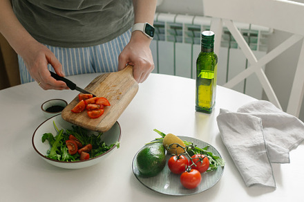 Woman preparing vegetable salad with tomato in the kitchen. Healthy food vegan, a Food & Drink Photo by Anikona
