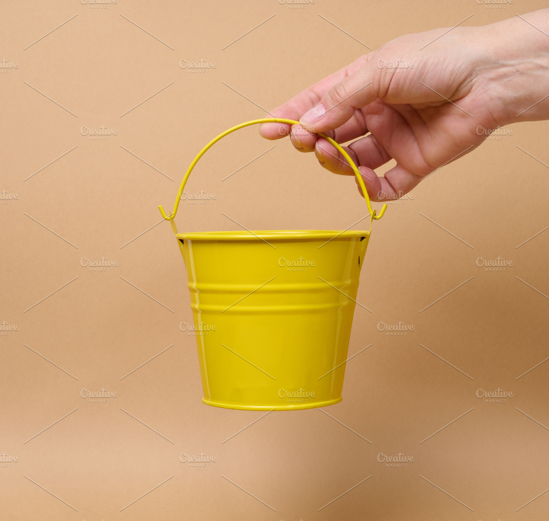A person holding a small yellow bucket by the handle against a b, a Person Photo by ndanko