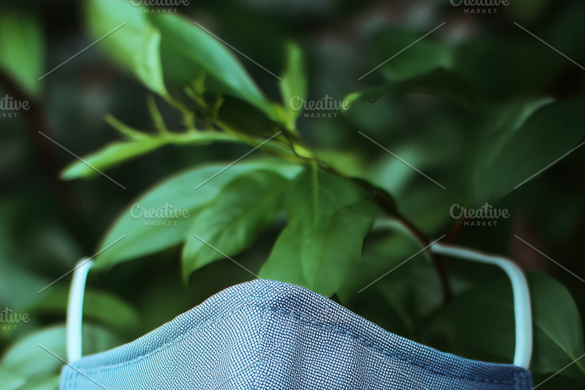 A blue fabric face mask mockup hanging against a backdrop of green leaves, a Mask Mockup by Textures & Backgrounds