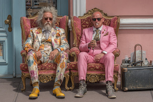 Two stylish men in colorful suits sit on ornate armchairs outsid, a Photo by AS photostudio