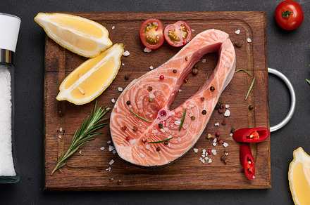 Raw salmon steak on a wooden cutting board, lemon slices, spices, a Food & Drink Photo by ndanko