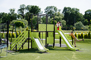 Children playing on a bright green playground structure on a sunny day outside, a Photo by AS photostudio