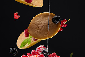 Pancakes fall on a stack of fritters with berries and mint, driz, a Food & Drink Photo by ndanko