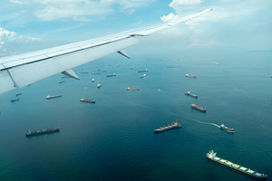 Airplane arriving over sea with cargo ships in Singapore, a Transportation Photo by GoodGoods