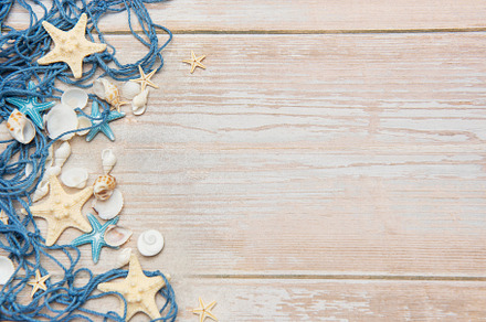 Fishing net, starfishes and seashells lying on wooden planks bac