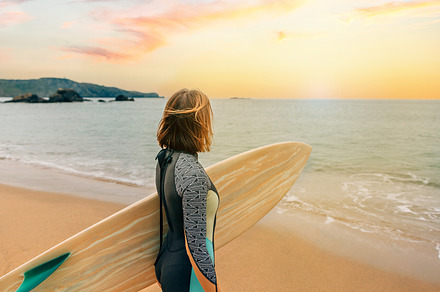 Surfer woman with wetsuit carrying surfboard looking to the sea at the beach, a Holiday Photo by davidpereiras