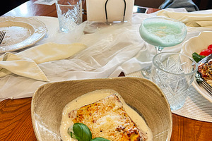 Elegant dining setup with lasagna dish, drink, and floral decoration on a table, a Photo by AS photostudio