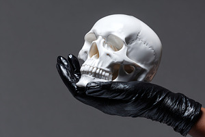 Holding a white skull with black gloves in a minimalistic background setting, a Holiday Photo by AlyaAnd