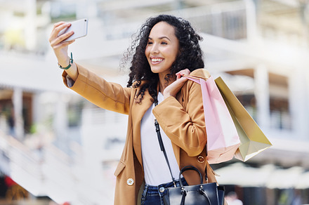 Fashion, shopping and woman taking a selfie in the city standing in the street. Black woman with shopping bags, phone in hand and taking a picture in retail shopping mall, happy from sale or discount, a Photo by Peopleimages.com