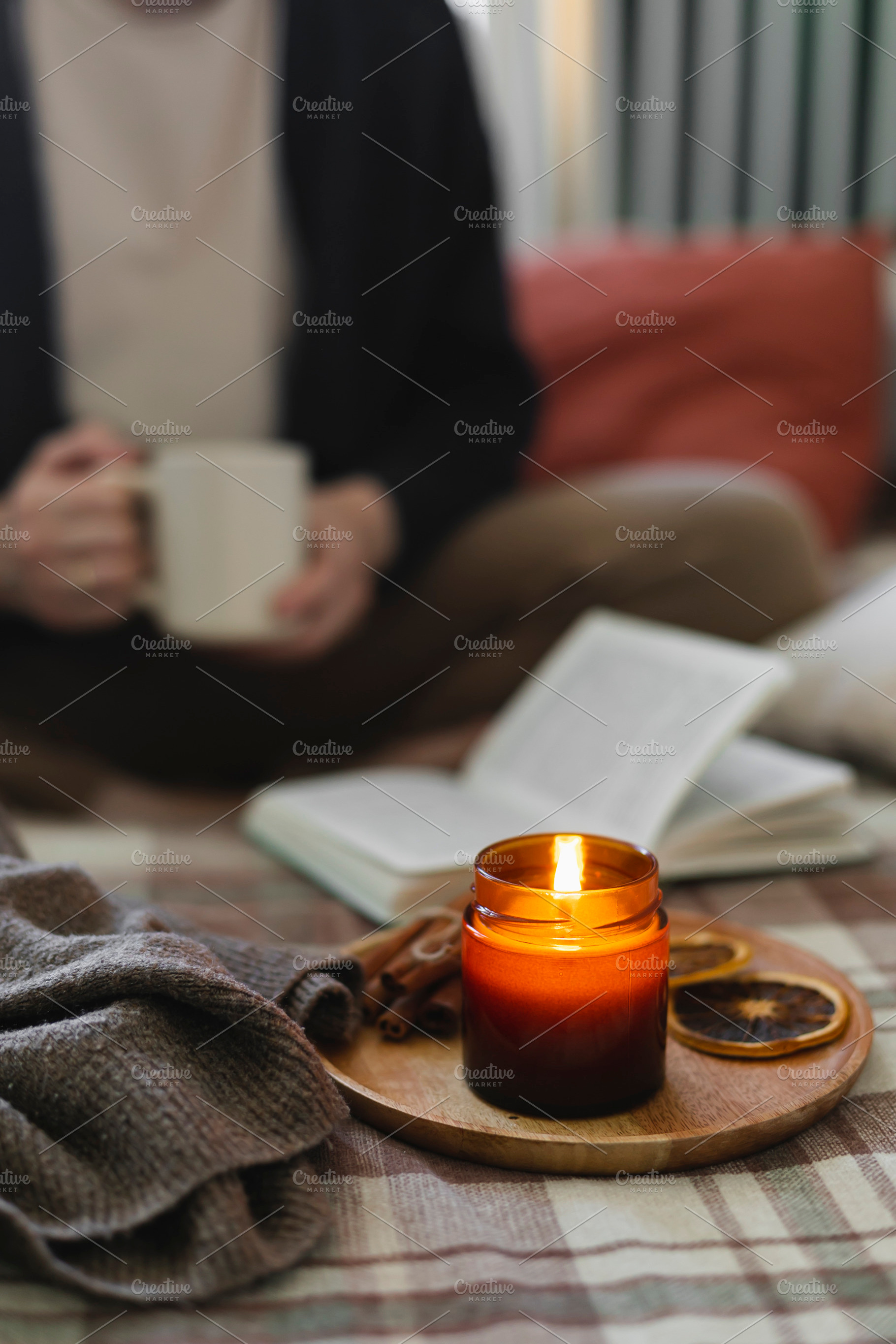 Burning candle on background of young woman holding mug coffee or tea, reading, a Beauty & Fashion Photo by Anikona