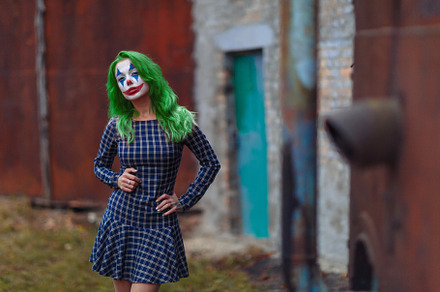 Portrait of a greenhaired girl in chekered dress with joker makeup on a rusty m