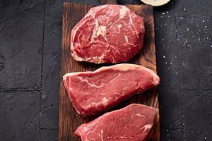 Raw rib-eye, roast beef, flank and rump steak displayed on a wooden board with, a Food & Drink Photo by Asya Nurullina