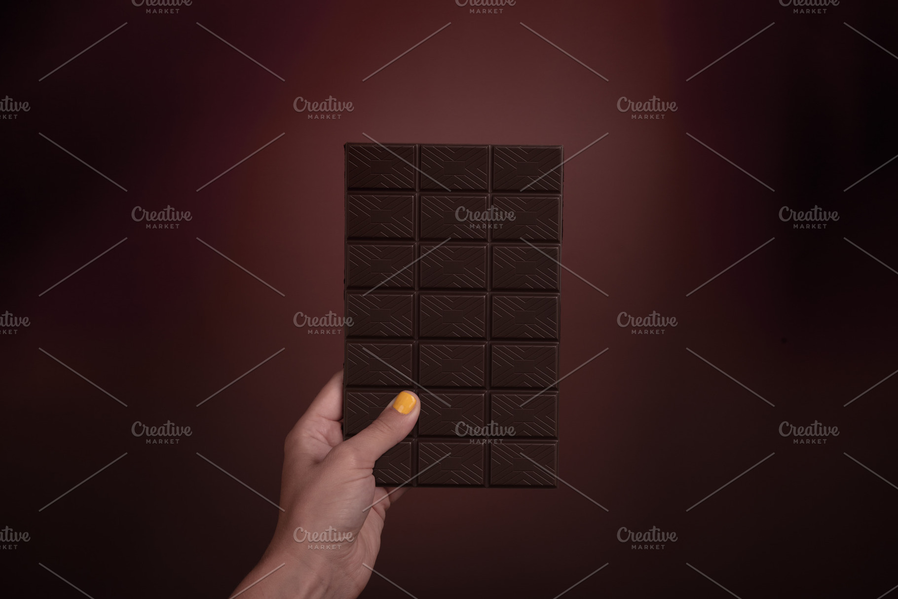 Female hand with yellow nail polish holding a dark chocolate bar, a Food & Drink Photo by Ales Munt