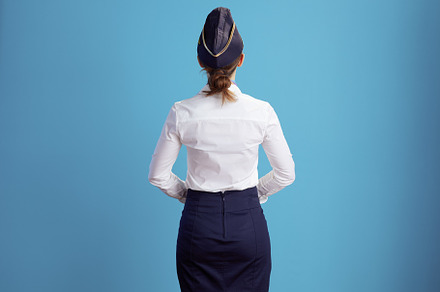 Seen from behind stylish air hostess woman on blue, a Business Photo by Alliance Images