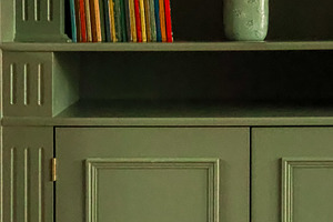 Bookshelf with colorful book spines and a vintage vase on a green wooden cabine, a Photo by Studio ANNA