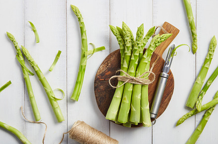 Peeling fresh green asparagus on wooden cutting board