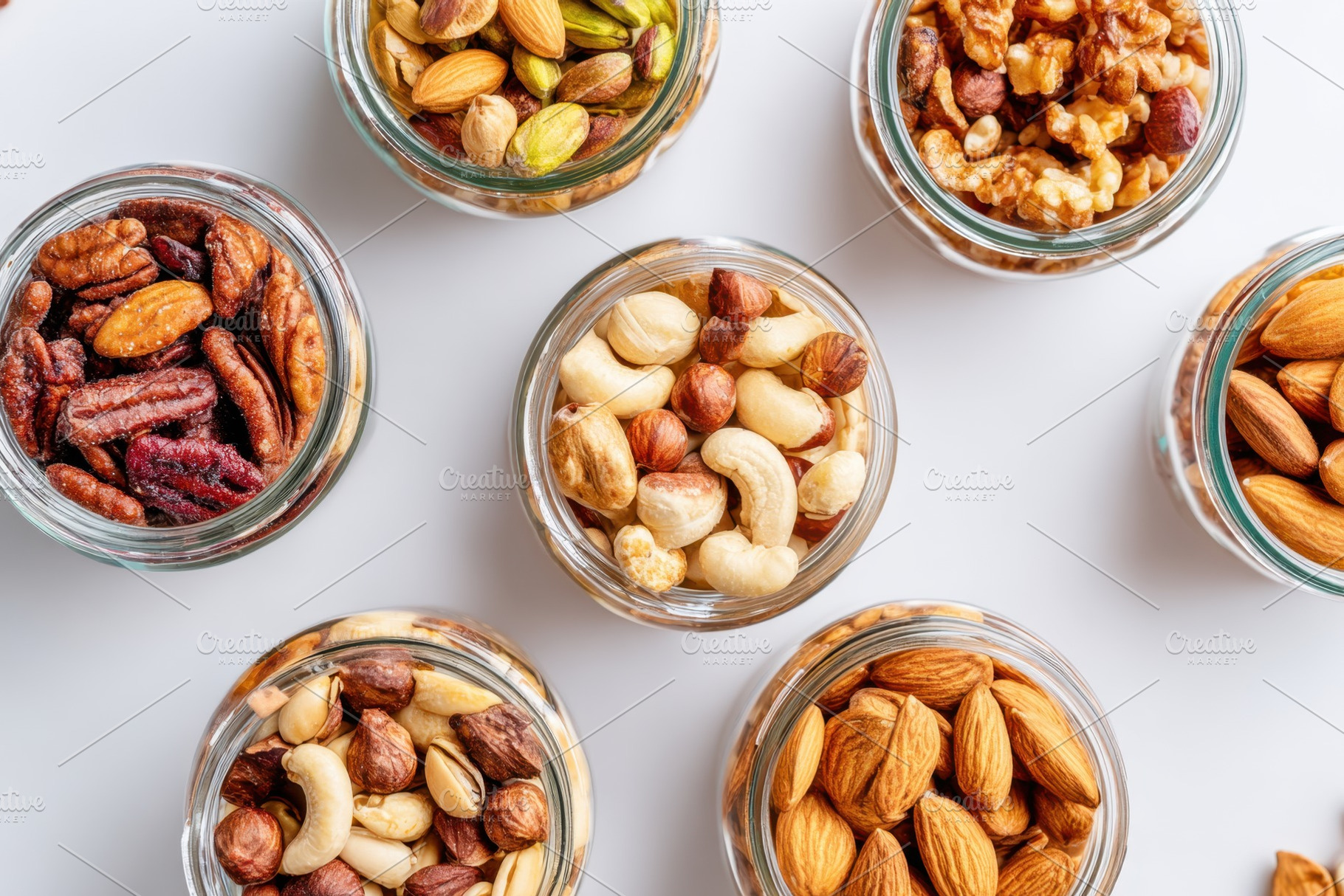 Assorted nuts in glass jars on white surface, a Food & Drink Photo by AlyaAnd