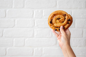 Hand Holding Raisin Danish Pastry Against White Brick Wall, a Food & Drink Photo by etorres69