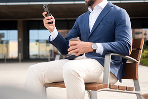 Businessman checking smartphone during coffee break outside office, a Business Photo by etorres69
