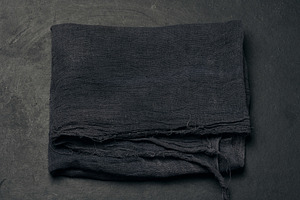 Folded black gauze kitchen napkin on black table, top view, a Food & Drink Photo by ndanko