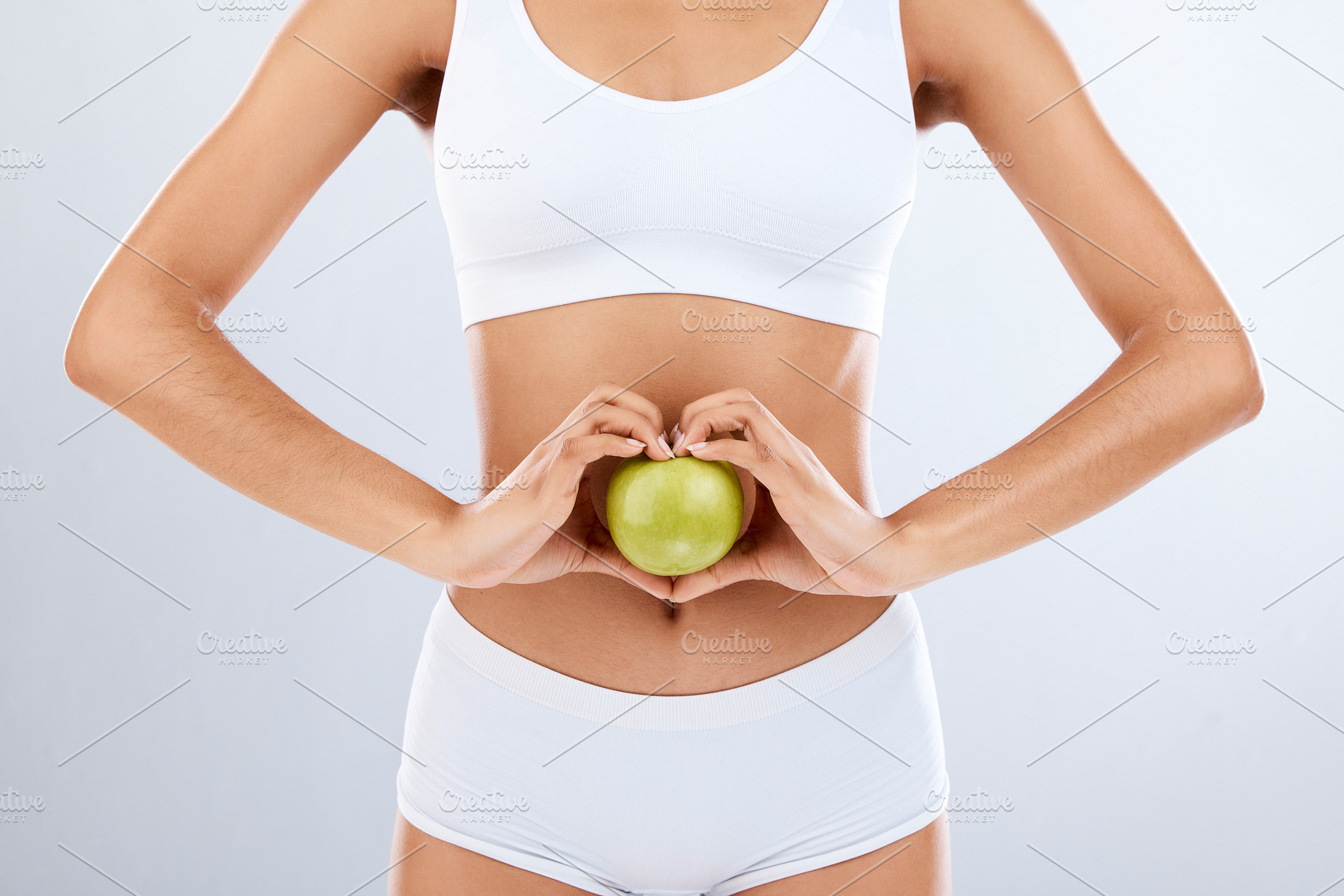 Digestion, apple and woman stomach with hands in heart shape for nutrition, detox diet and studio background. Fruits, wellness and healthy abdomen body with care, love and lose weight for strong gut, a Photo by Peopleimages.com