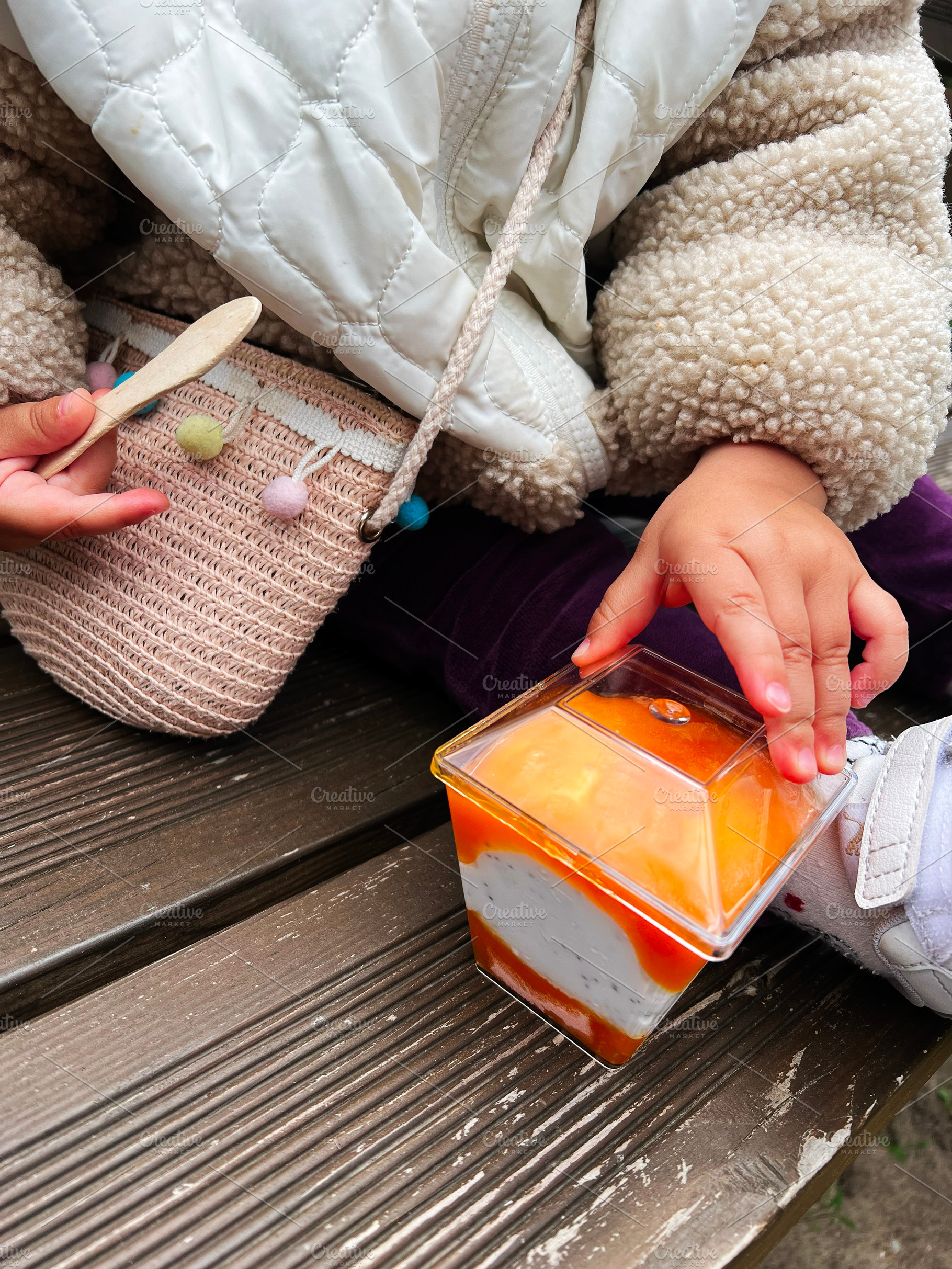 Child holding dessert with caramel topping on a wooden bench outdoors, a Photo by AS photostudio