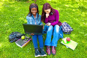Two students using laptop and smartphone sitting on grass in a park, a Person Photo by Antonio Gravante Market