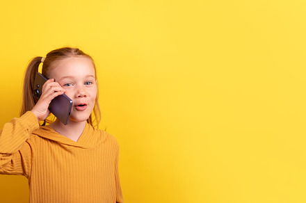 Smiling young girl with pigtails in a mustard sweater talking on