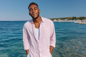 Man wearing a striped shirt smiles at the camera by the sea on a sunny day, a Person Photo by AlyaAnd