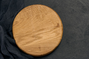 Empty round brown wooden cutting board on a black background, a Food & Drink Photo by ndanko