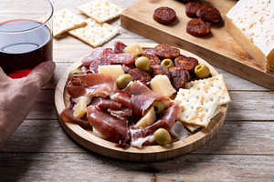 Hand picking up glass of red wine beside Spanish charcuterie board, a Food & Drink Photo by etorres69