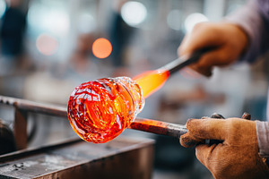 Craftsman shaping molten glass in vibrant colors, an Industrial Photo by AlyaAnd