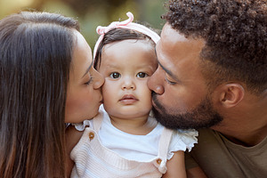 Mother, father and baby face kiss while bonding in a garden outdoors with love, care and affection. Loving, caring parents kissing little daughter while bond in nature for calm relaxation, a Photo by Peopleimages.com