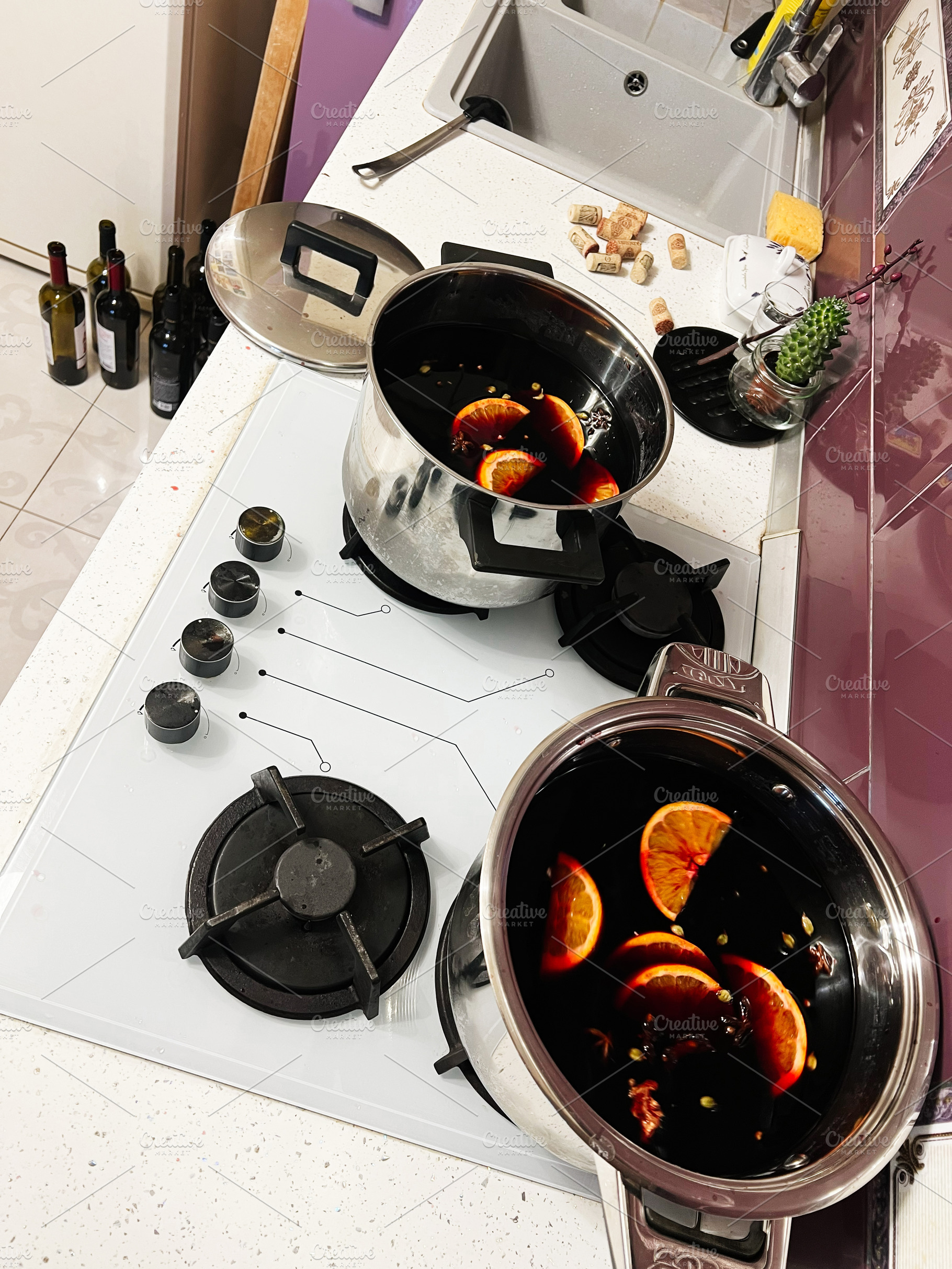 Two pots simmering mulled wine with orange slices in a cozy modern kitchen, a Photo by AS photostudio
