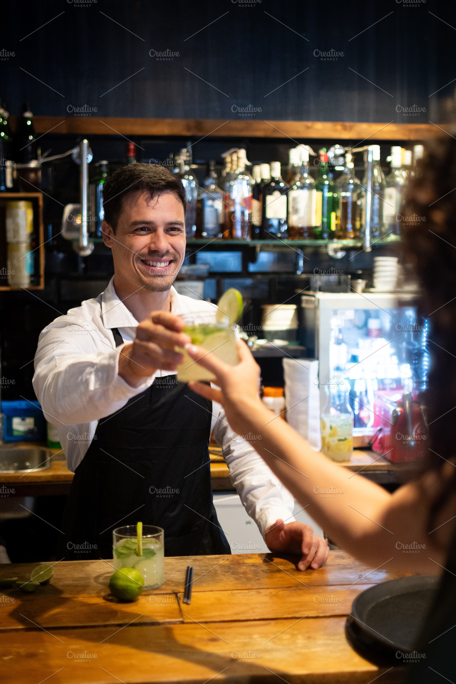Smiling bartender serving cocktail to customer at modern restaurant bar, a Person Photo by etorres69