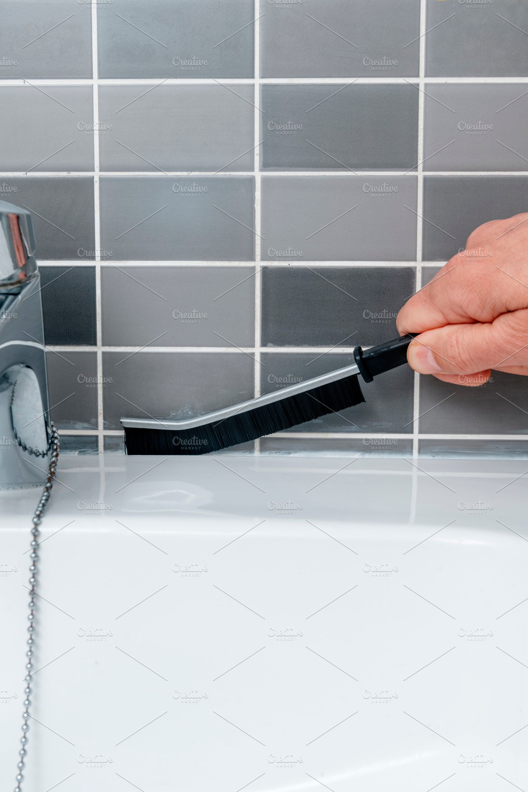 a man scrubs the joints along the sink tiles, a Photo by Nito