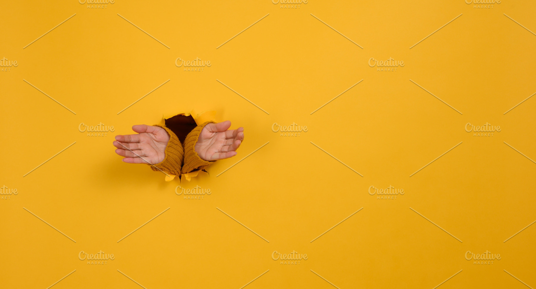 Two female hands in yellow sleeves peek out from a torn hole in, a Person Photo by ndanko